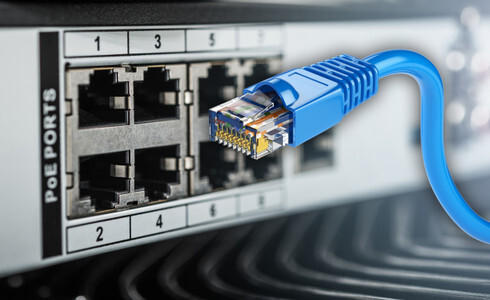 A close-up of an Ethernet patch panel showing multiple RJ45 ports with yellow and blue copper cables plugged in, highlighting the infrastructure used to deliver both data and electrical power to networked devices.