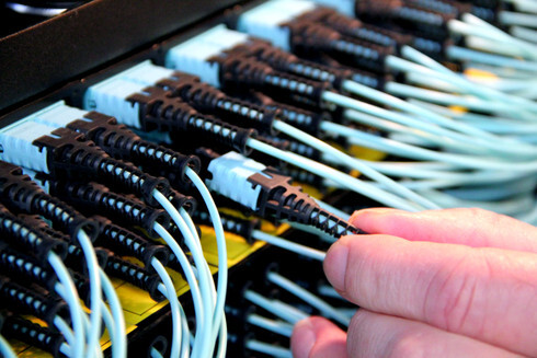 A technician's hand organizing a dense bundle of aqua-colored MTP/MPO fiber trunk cables, demonstrating the professional cable management needed for reliable high-speed switch-to-switch connections.