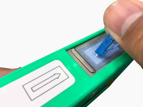A close-up of a technician using a specialized click-style fiber cleaning tool on a patch panel port to ensure a contaminant-free connection for optimal signal performance.