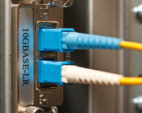A close-up of a compact LC fiber optic loopback adapter with a translucent blue housing, illustrating the tool used by technicians to test transceiver ports and network continuity