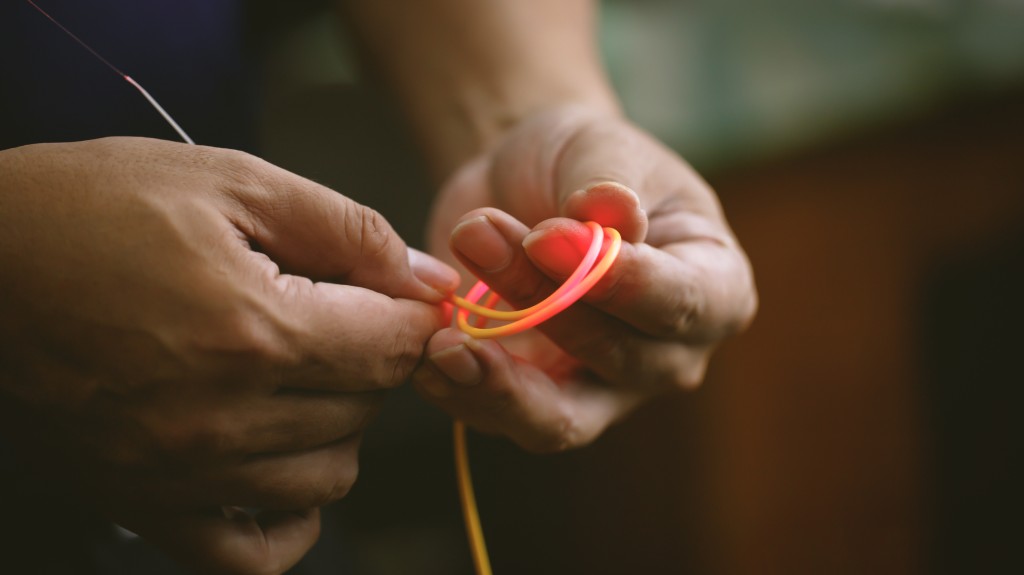 Hands bending a glowing fiber optic cable to demonstrate proper bend radius and signal transmission