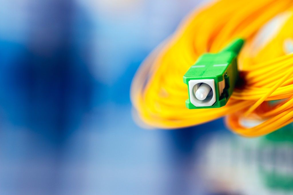 A close-up image of an Angled Physical Contact (APC) singlemode fiber optic patch cable, identifiable by its green connector housing and yellow fiber optic cable jacket. The image visually distinguishes the APC connector type.