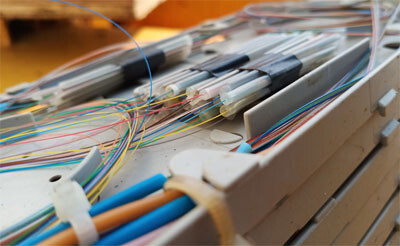 A precision fusion splicing machine in action, showing two fiber optic strands being aligned and joined by an electric arc to create a permanent, low-loss connection.