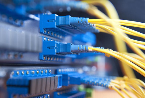 A row of consistent, high-quality blue fiber optic connectors and yellow cabling, illustrating the importance of component uniformity in a data center.